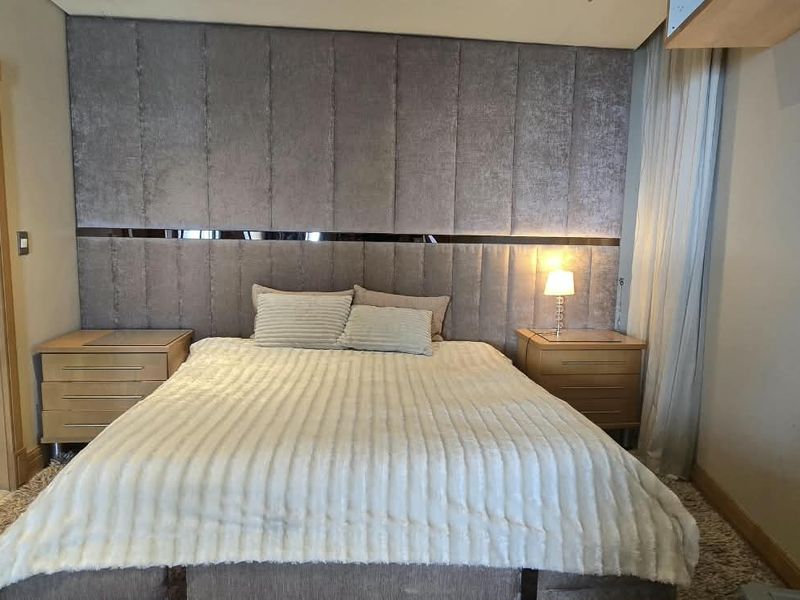 A well-appointed bedroom featuring a large upholstered headboard wall panel, recessed ceiling lighting, and direct access to an en-suite bathroom.
