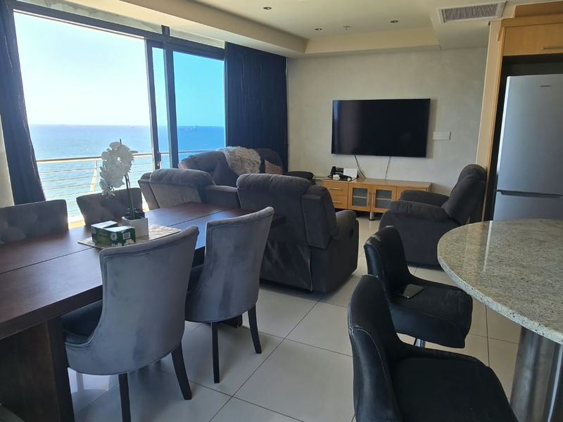 Open-plan living and dining area featuring tiled floors, a granite breakfast bar, and large sliding doors opening to a scenic ocean view.