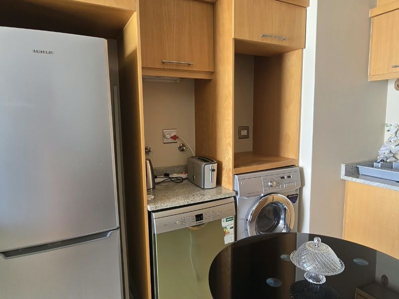 Compact kitchen area featuring light wood cabinetry, granite countertops, stainless steel sink, and integrated appliances including a dishwasher and washing machine.