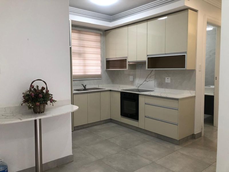 Modern kitchen featuring sleek cream cabinetry, stone countertops, integrated oven, electric cooktop, and marble-look splashback with neutral tiled flooring.