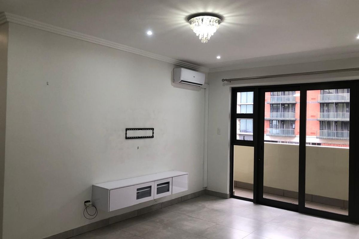 A bright, modern living room featuring tiled floors, a wall-mounted media console, air conditioning, and sliding glass doors leading to a balcony.