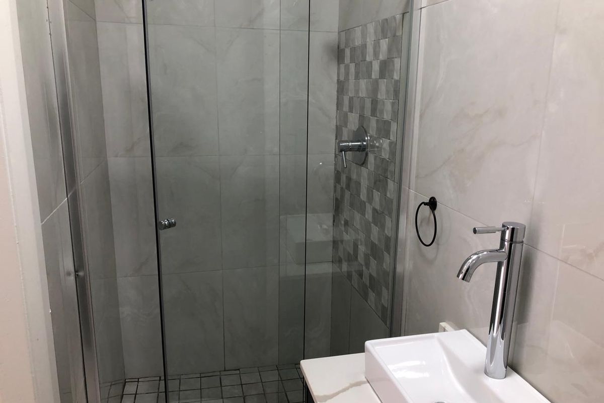 A modern bathroom featuring a glass-enclosed shower, contemporary vessel sink with a chrome mixer tap, and neutral wall and floor tiling.