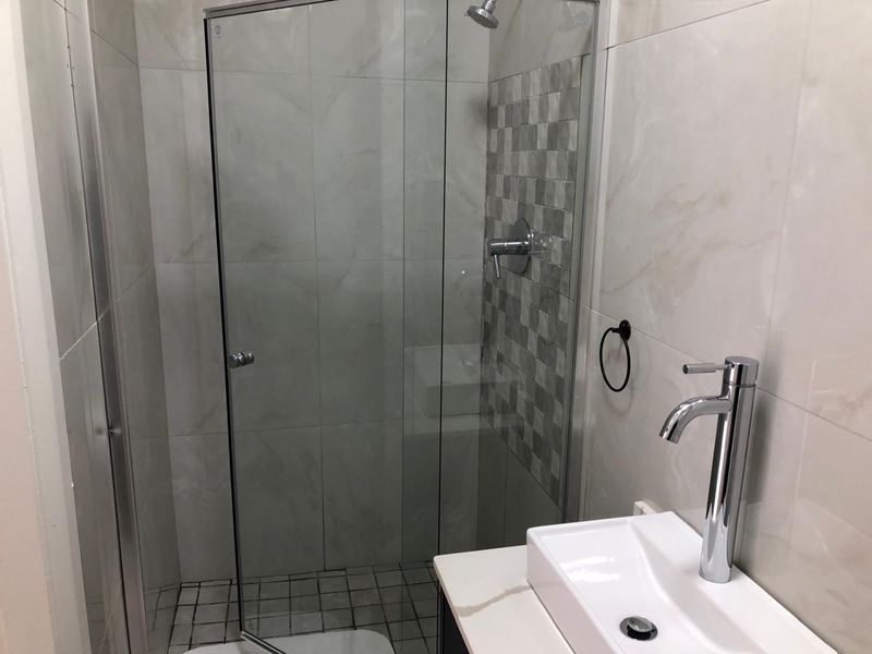 A modern bathroom featuring a glass-enclosed shower, contemporary vessel sink with a chrome mixer tap, and neutral wall and floor tiling.