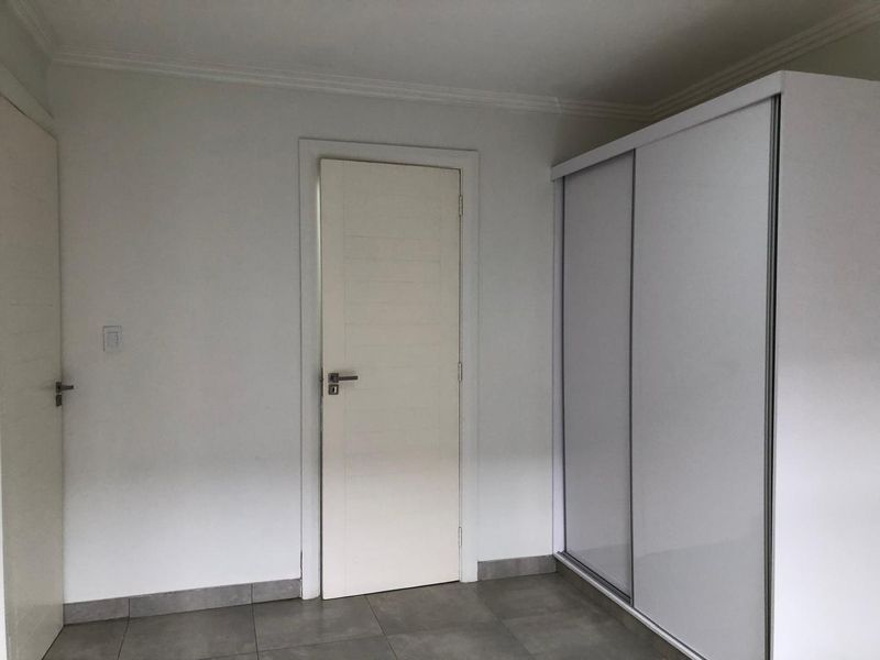 A clean, neutral bedroom featuring large-format floor tiles, a built-in sliding door wardrobe, and crisp white walls.