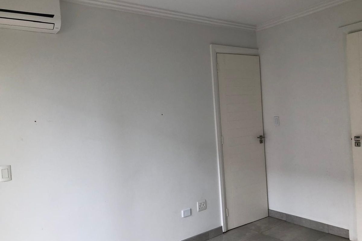A clean, empty bedroom featuring tiled flooring, coving, and a wall-mounted split-system air conditioning unit.