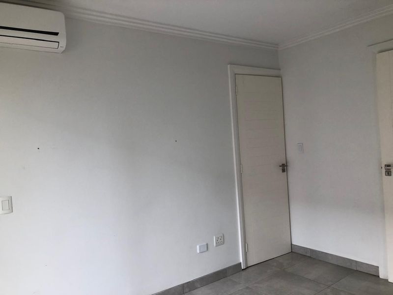 A clean, empty bedroom featuring tiled flooring, coving, and a wall-mounted split-system air conditioning unit.