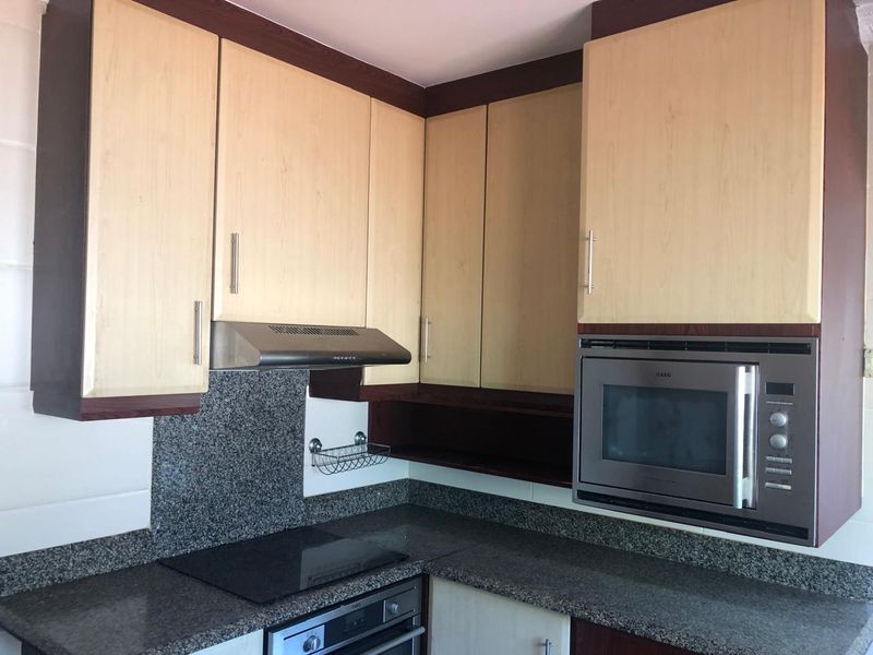 A functional kitchen featuring granite countertops, built-in cabinetry, and integrated appliances including an oven, hob, extractor fan, and microwave.