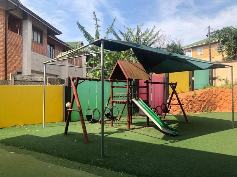 A communal garden area featuring artificial turf, a shaded playground structure, and perimeter boundary walls.