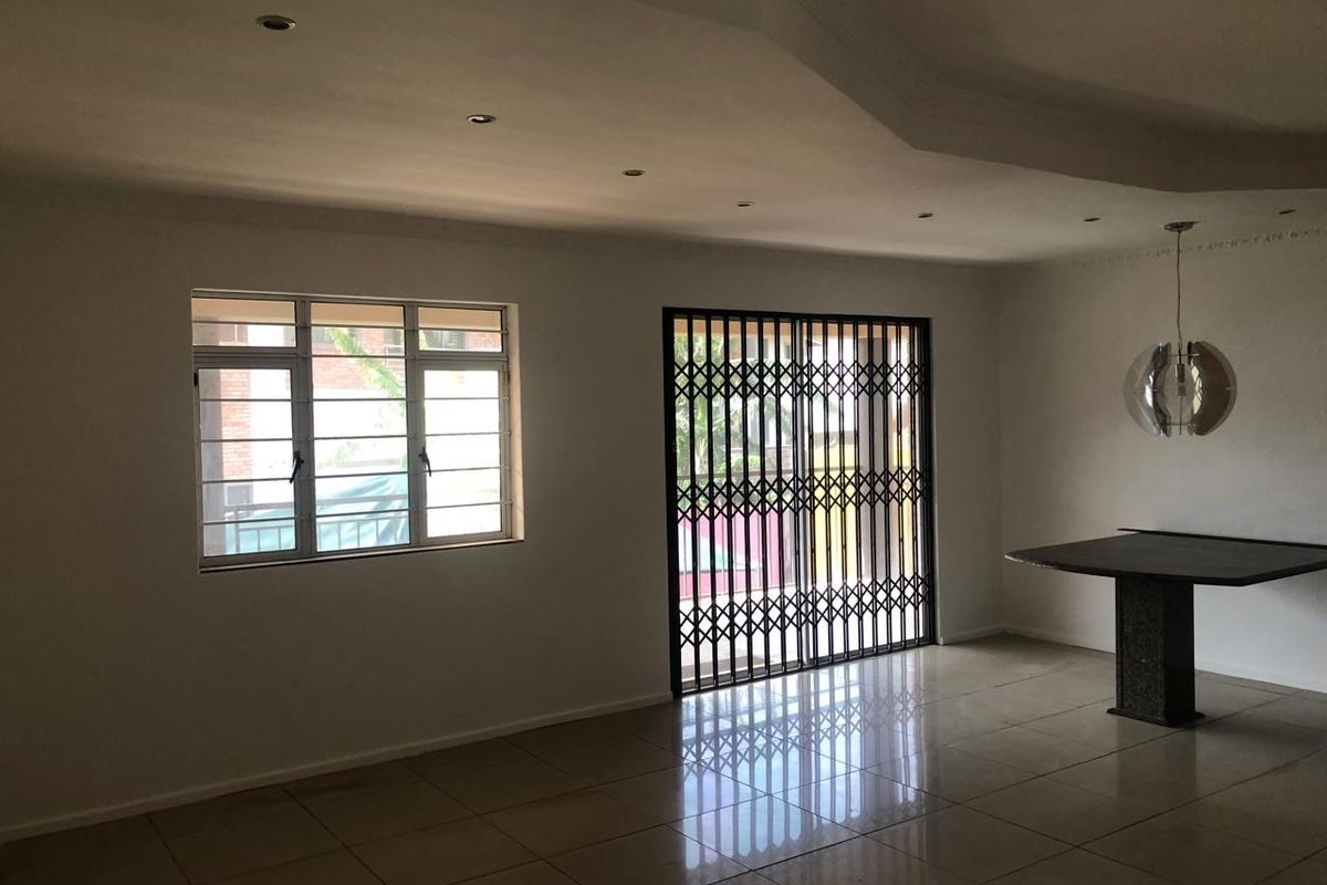 Spacious living area featuring tiled flooring, recessed ceiling lighting, and a secure sliding door with a metal security gate.