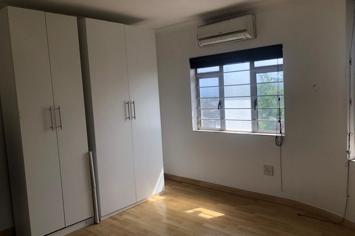 A bright, empty bedroom featuring built-in cupboards, laminate flooring, and an air conditioning unit, offering a clean canvas for personalization.