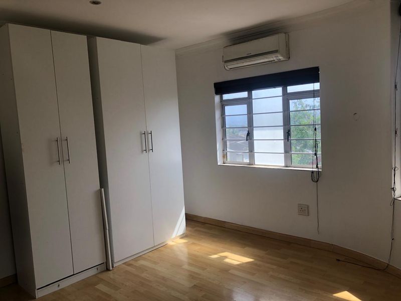 A bright, empty bedroom featuring built-in cupboards, laminate flooring, and an air conditioning unit, offering a clean canvas for personalization.