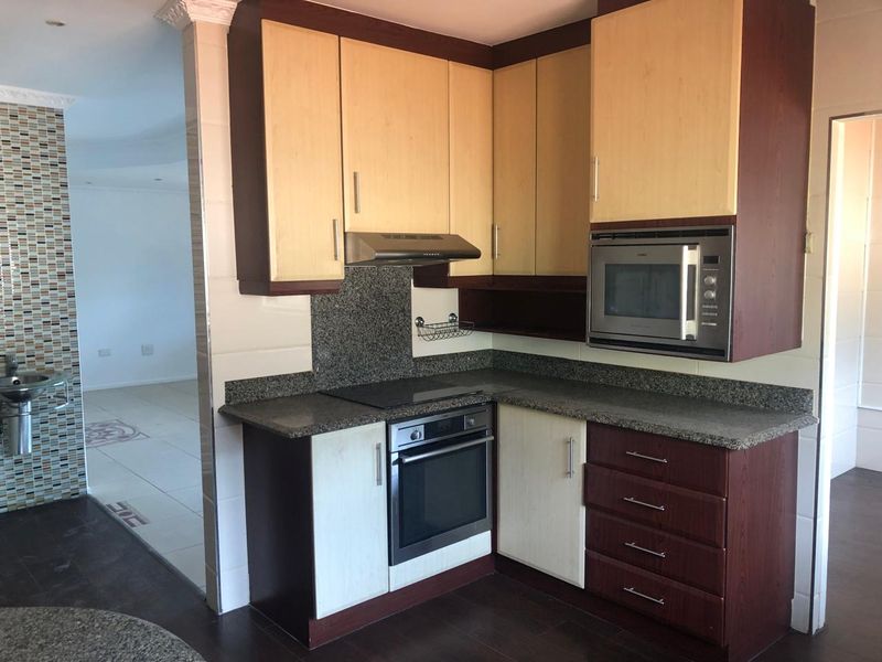 A functional kitchen featuring granite countertops, built-in oven, hob, extractor fan, and integrated microwave with two-tone cabinetry.