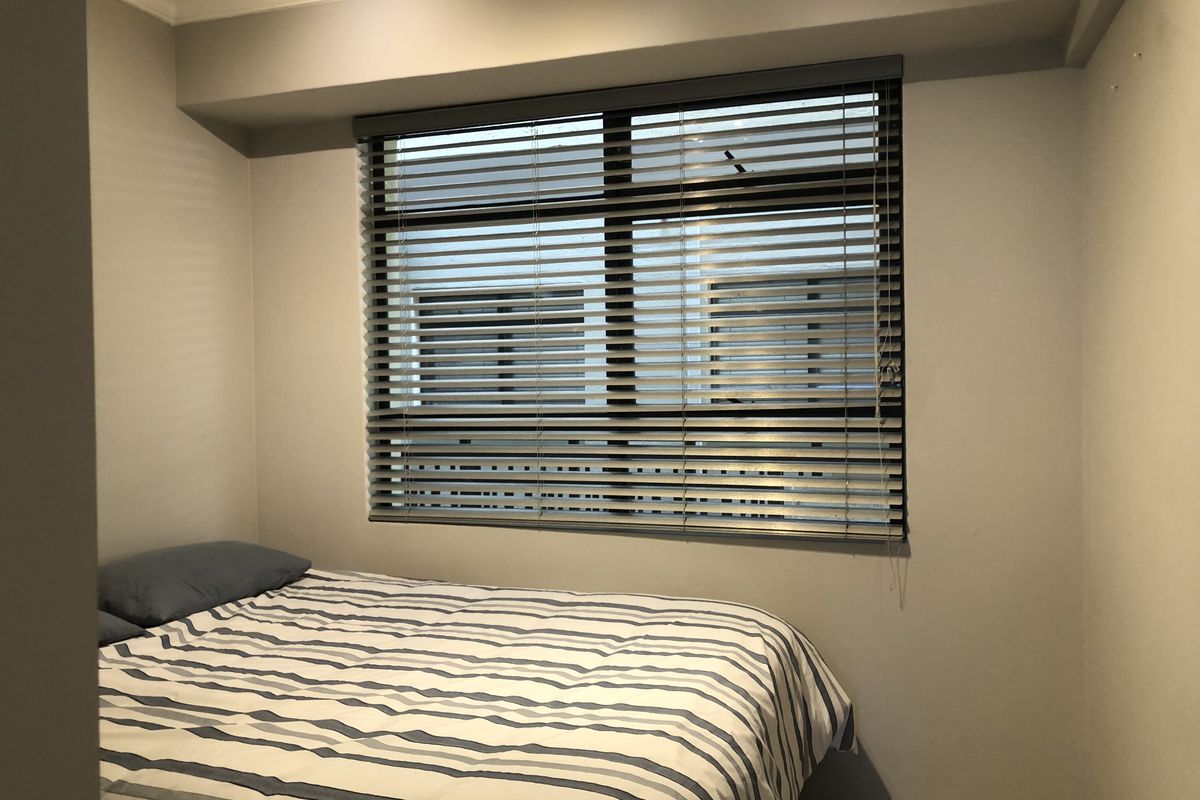 A compact bedroom featuring neutral walls, a window with fitted venetian blinds, and decorative ceiling coving.
