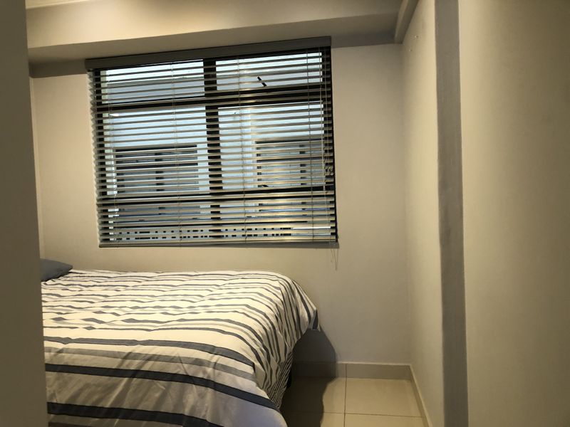 A compact bedroom featuring tiled flooring and a window fitted with venetian blinds.