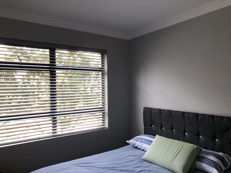 A well-maintained bedroom featuring neutral grey walls, coving, and fitted venetian blinds allowing natural light.