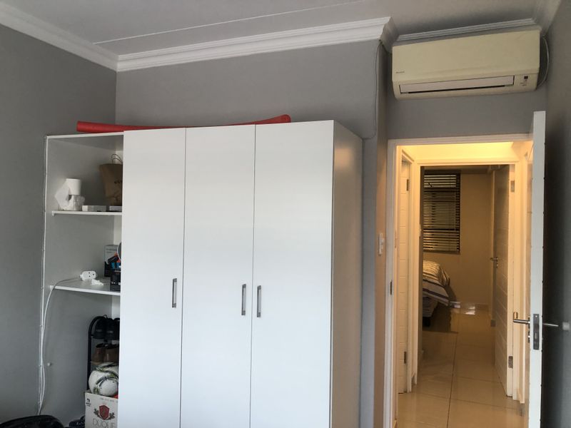 Bedroom featuring a built-in wardrobe, split-system air conditioning unit, and tiled flooring, with a doorway leading to an adjacent room.