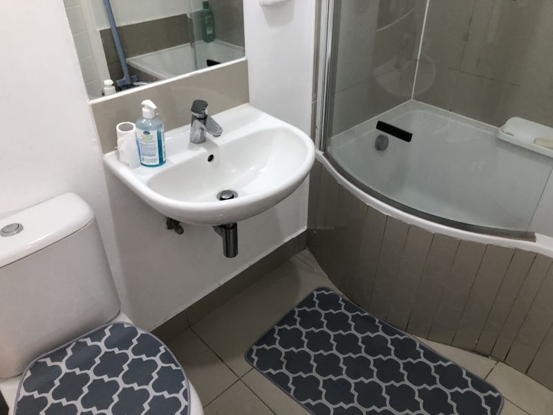 Compact bathroom featuring a wall-mounted basin, toilet, and a curved shower enclosure with tiled finishes.