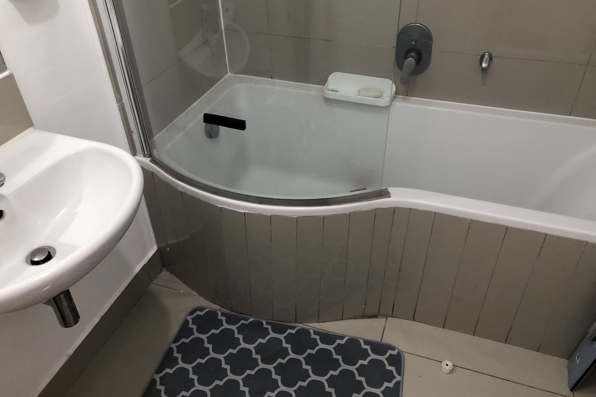 A functional bathroom featuring a curved bathtub with a glass shower screen and a wall-mounted basin with chrome fixtures.