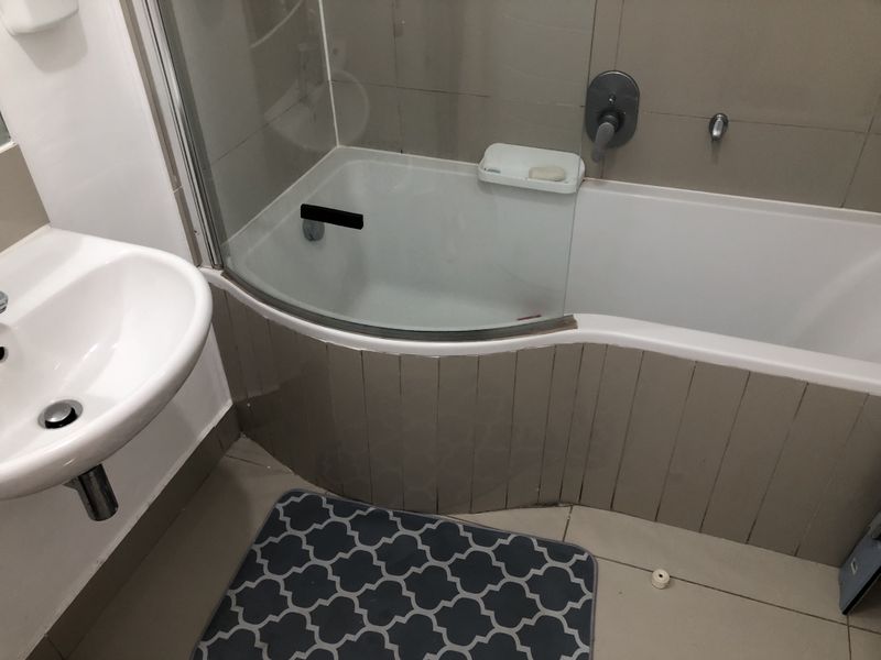A functional bathroom featuring a curved bathtub with a glass shower screen and a wall-mounted basin with chrome fixtures.