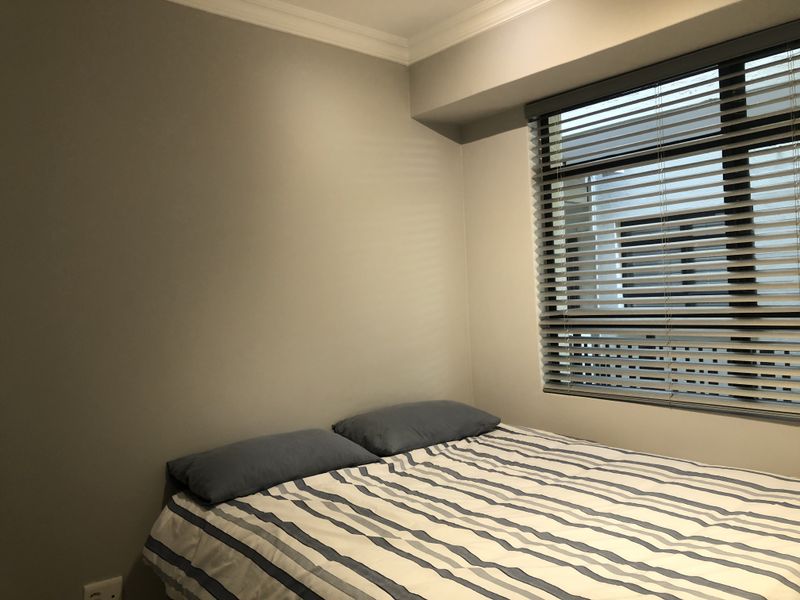 A cozy bedroom featuring neutral wall tones, crown molding, and fitted venetian blinds, providing a clean and functional space.