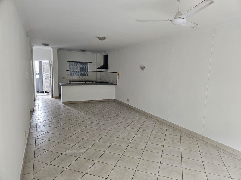 Spacious open-plan living and kitchen area featuring tiled flooring, a ceiling fan, and a functional kitchen layout with a breakfast bar.