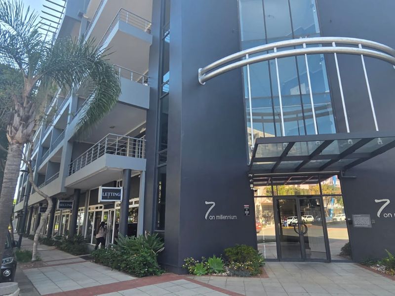 Modern apartment building exterior featuring a glass entrance canopy, dark facade, and balconies overlooking the street.