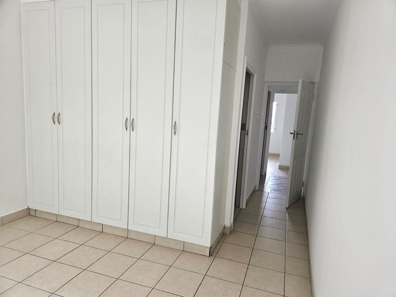 A clean, empty bedroom featuring white built-in cupboards and neutral tiled flooring, leading into a hallway with access to other rooms.