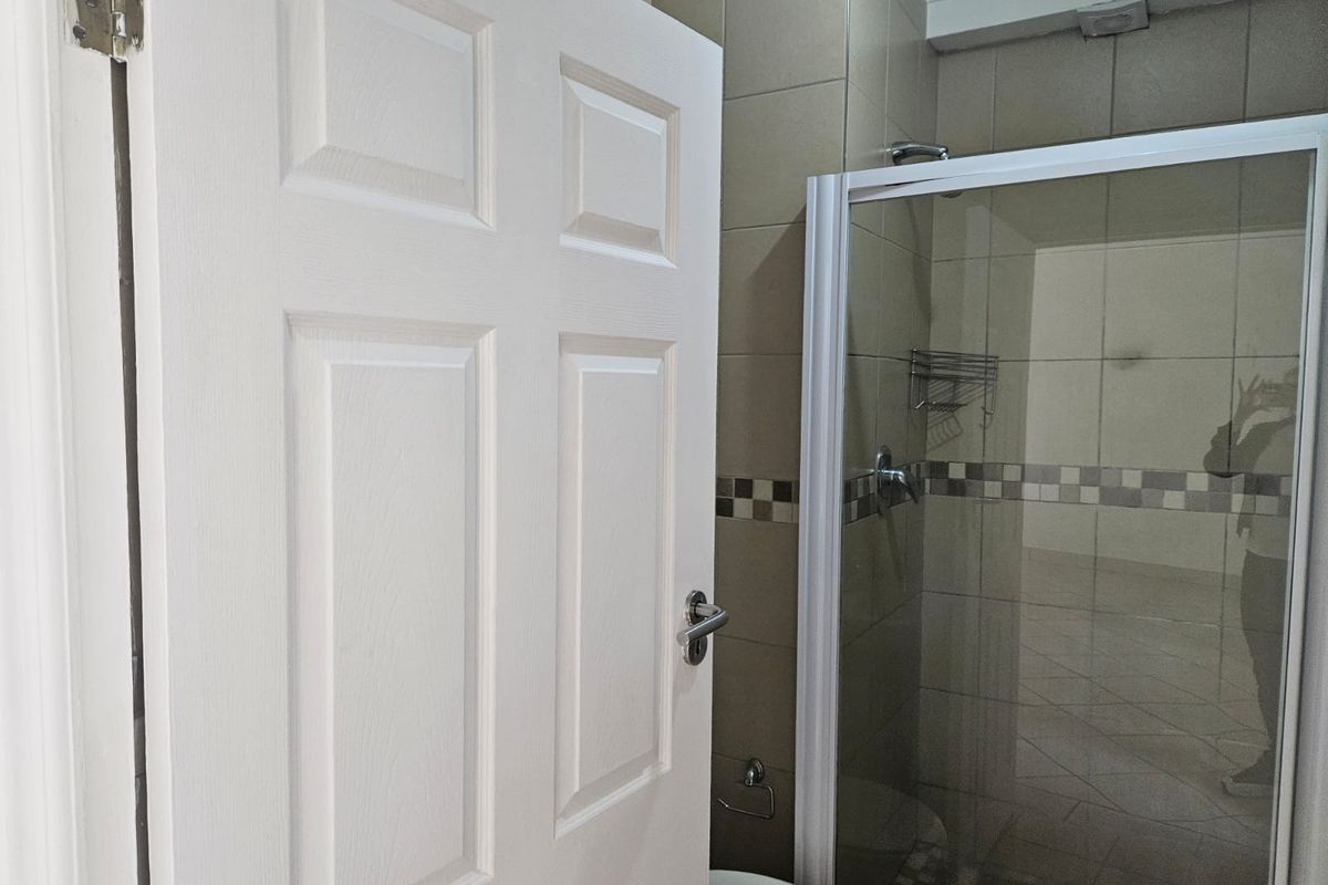 A functional bathroom featuring a glass-enclosed shower, neutral wall tiling with a decorative border, and tiled flooring.