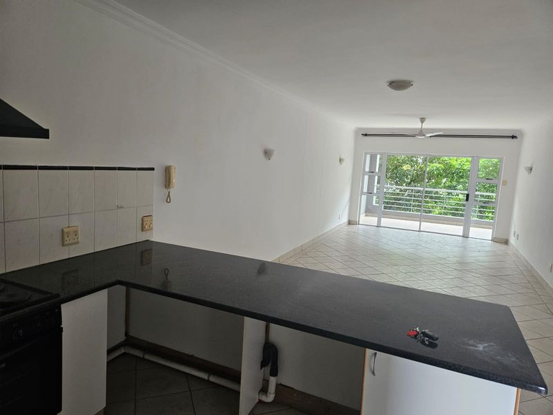 Open-plan kitchen and living area featuring granite countertops, built-in appliances, and tiled flooring, leading to a balcony with natural light.