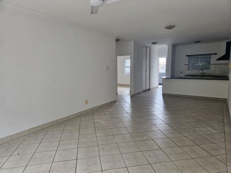 Spacious open-plan living and kitchen area featuring neutral tiled flooring, a breakfast bar, and built-in cabinetry, offering a versatile layout for modern living.