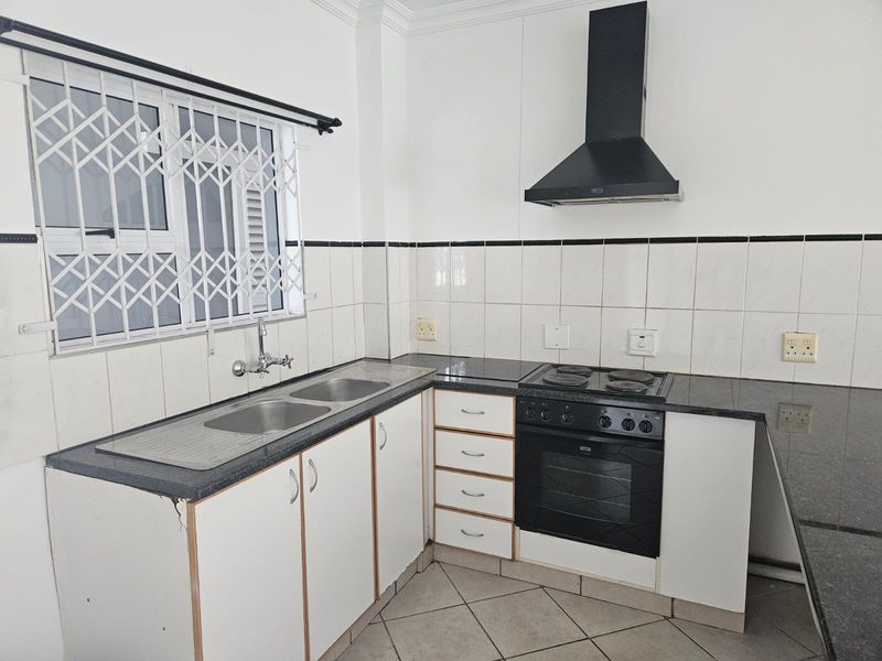A functional kitchen featuring granite countertops, built-in oven, electric hob, extractor fan, and double sink with tiled backsplash and security window bars.