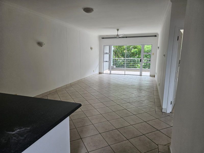 Spacious open-plan living area featuring neutral tiled flooring, a ceiling fan, and large sliding glass doors providing access to a private balcony.