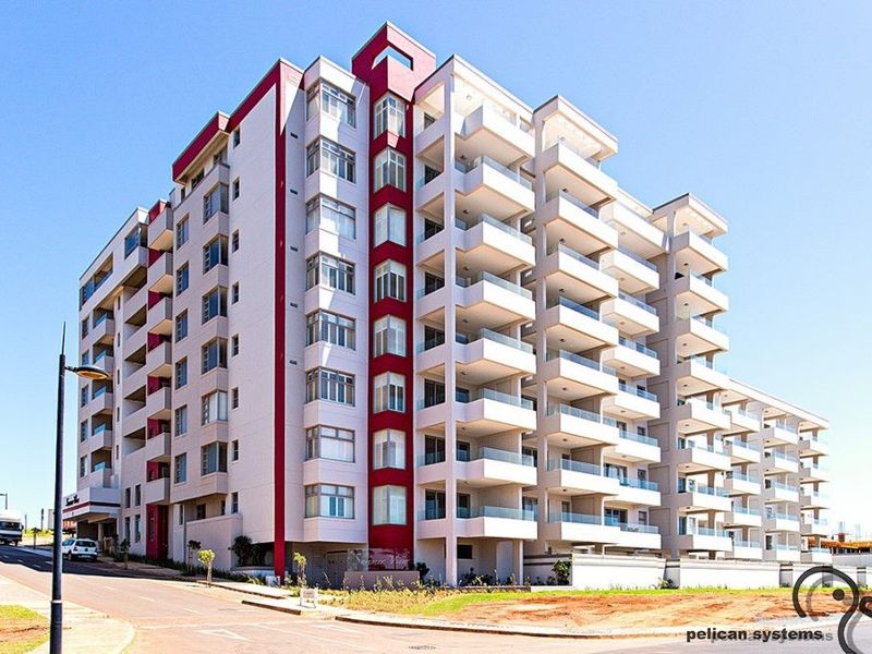 A modern multi-story apartment building featuring clean architectural lines, prominent red accents, and private balconies with glass balustrades.