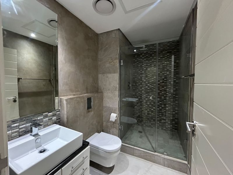 Modern bathroom featuring a glass-enclosed shower with mosaic tiling, a wall-mounted toilet, and a contemporary vessel sink vanity.