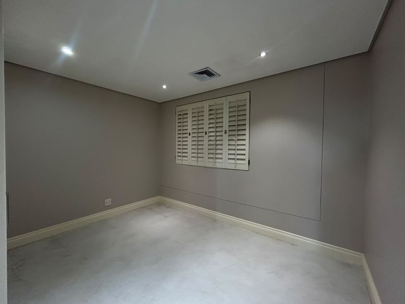 A clean, empty bedroom featuring neutral walls, recessed downlighting, and white plantation shutters, providing a versatile space ready for personalization.