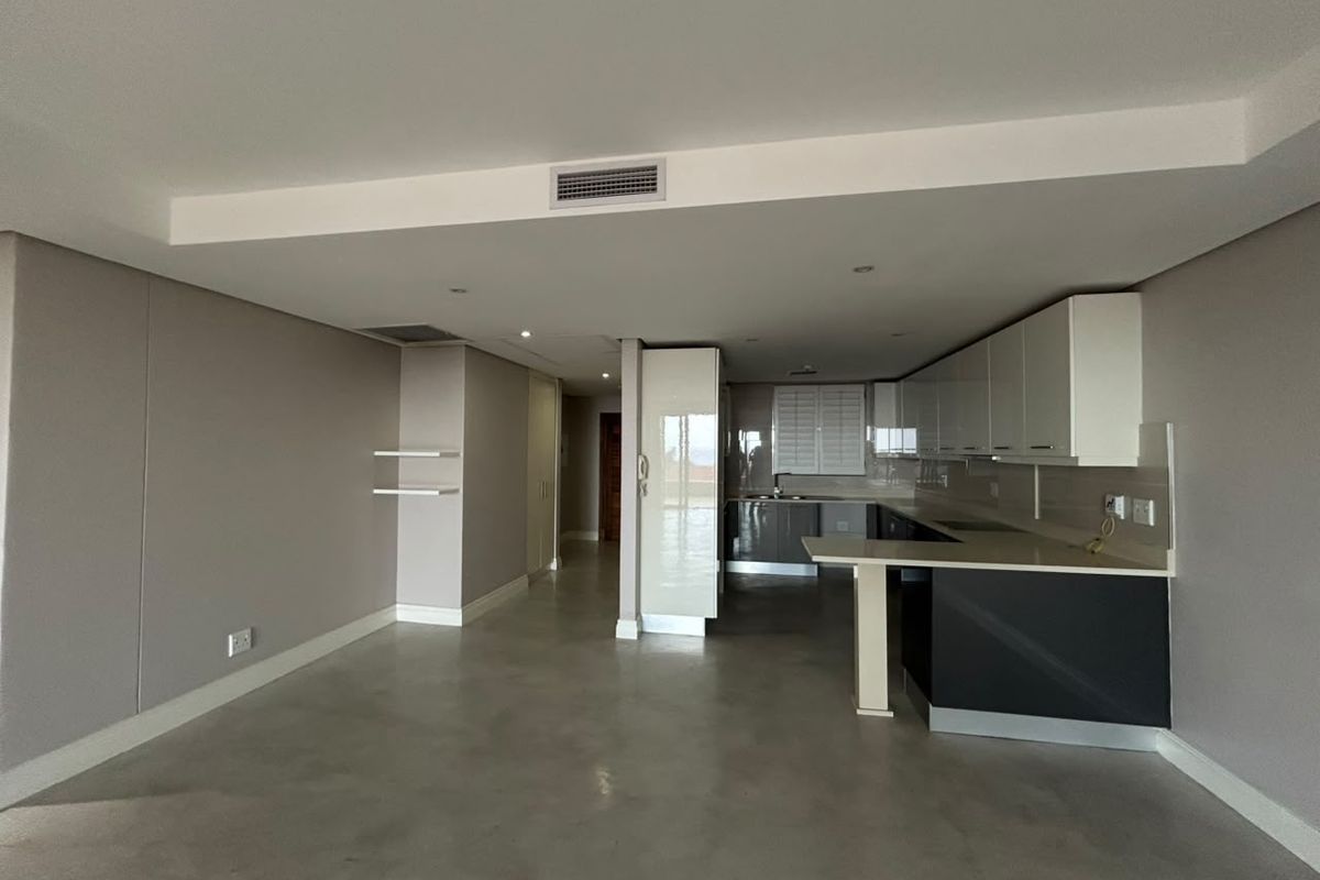 Spacious open-plan living and kitchen area featuring polished concrete floors, modern cabinetry, stone countertops, and integrated ducted air conditioning.