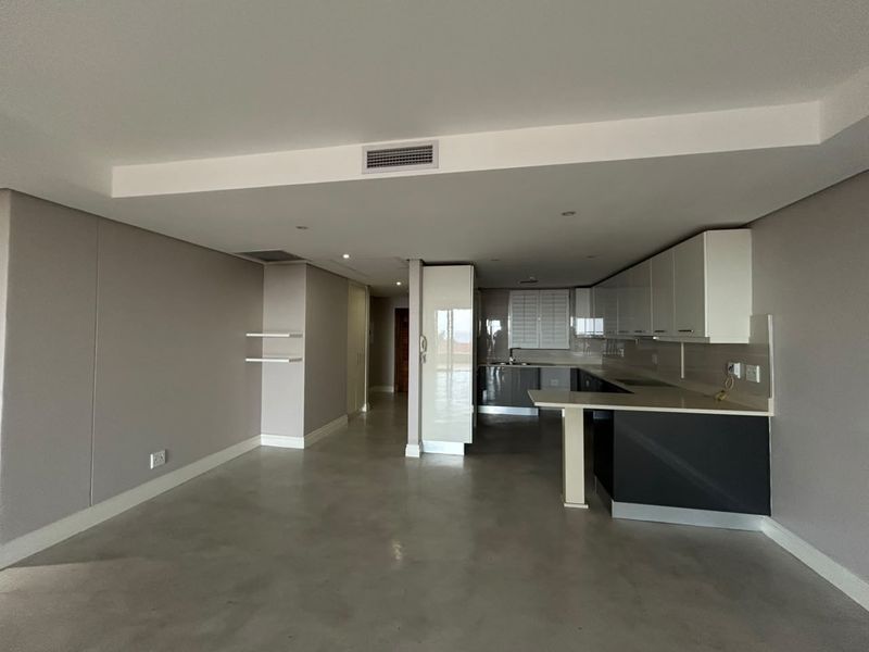 Spacious open-plan living and kitchen area featuring polished concrete floors, modern cabinetry, stone countertops, and integrated ducted air conditioning.