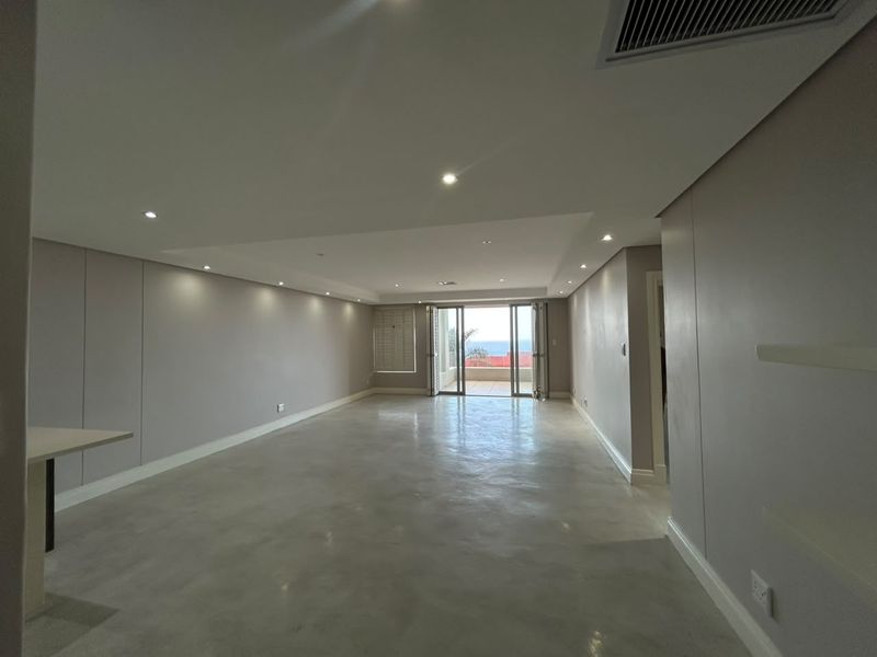 Spacious open-plan living area featuring polished concrete floors, recessed lighting, and bi-fold doors leading to an outdoor balcony with ocean views.