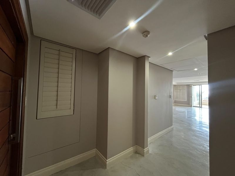A bright, modern hallway featuring polished concrete floors, recessed downlights, and plantation shutters, leading into an open-plan living area.