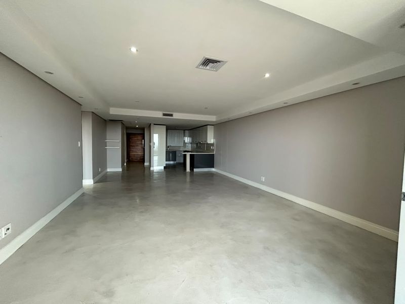 Spacious open-plan living area featuring polished concrete floors, recessed lighting, and a modern kitchen with built-in cabinetry and an island.