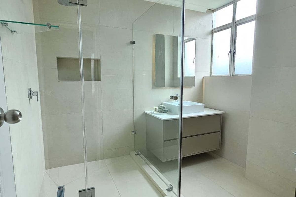 Modern bathroom featuring a glass-enclosed shower, wall-mounted vanity with vessel sink, and neutral floor-to-ceiling tiling.
