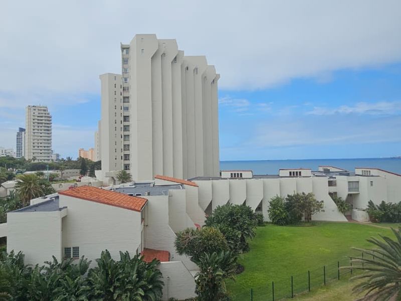 Elevated view overlooking the coastal apartment complex, surrounding landscaped grounds, and the ocean horizon.