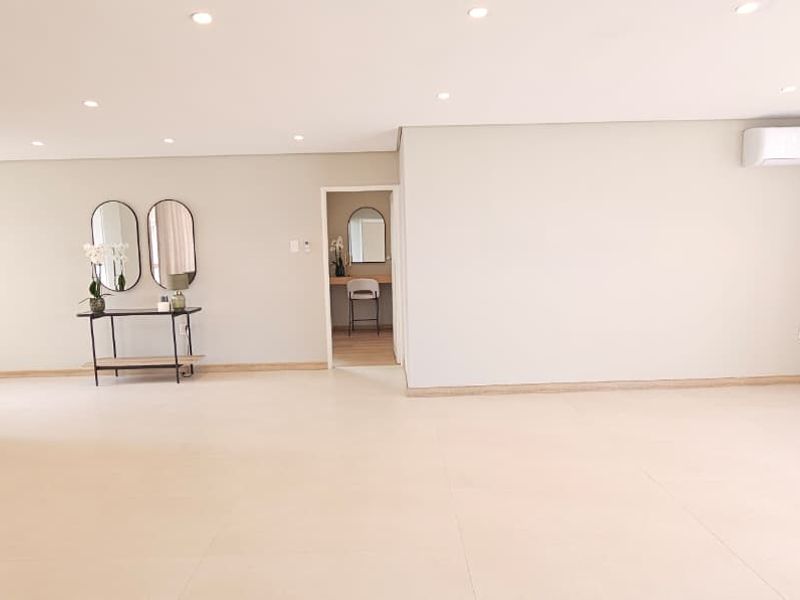 Spacious open-plan living area featuring neutral tiled flooring, recessed downlighting, and a wall-mounted air conditioning unit, offering a bright and modern atmosphere.