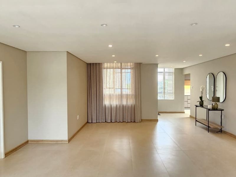 Spacious and bright open-plan living area featuring neutral tiled flooring, recessed downlighting, and clean finishes, offering a versatile space for modern living.