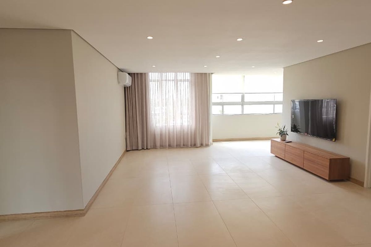 Spacious living area featuring neutral tiled flooring, recessed downlighting, and an integrated air conditioning unit, offering a bright and clean open-plan layout.