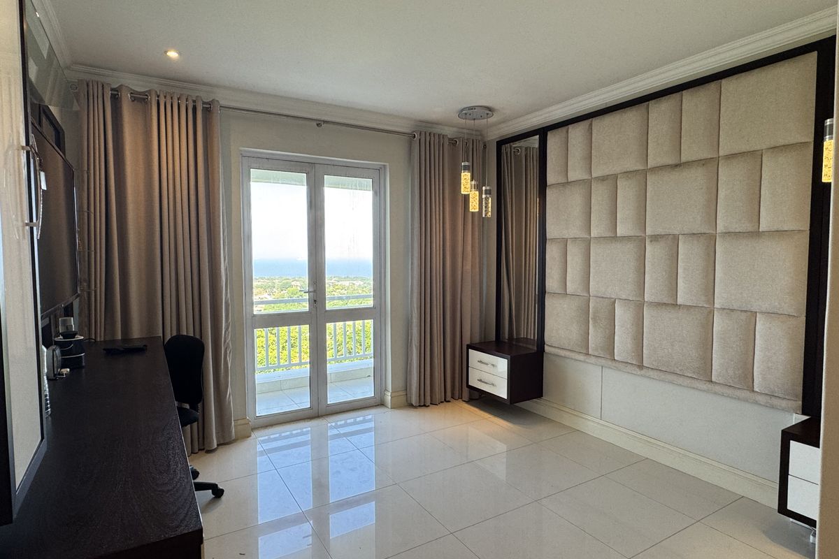 A well-maintained bedroom featuring modern upholstered wall paneling, floating cabinetry, polished tile floors, and direct access to a private balcony with scenic views.
