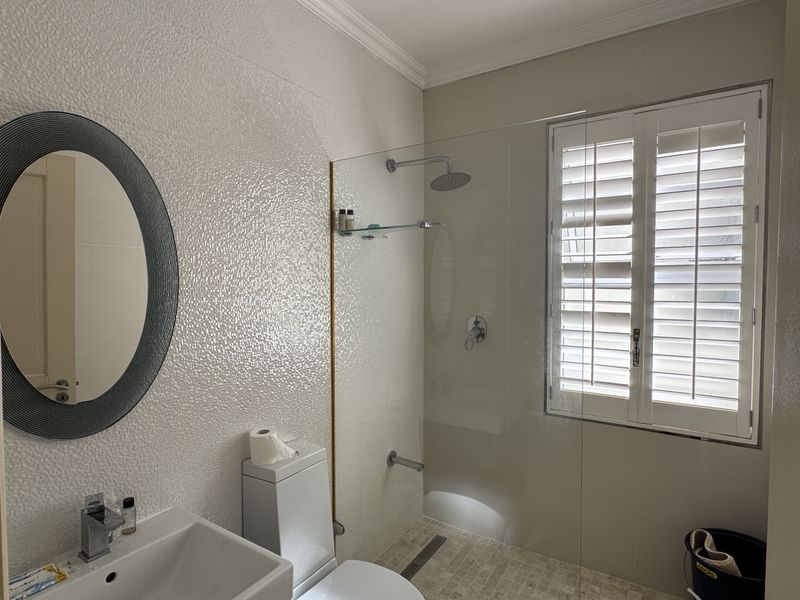 Modern bathroom featuring a walk-in shower with a rain shower head, wall-mounted basin, and plantation shutters for privacy.
