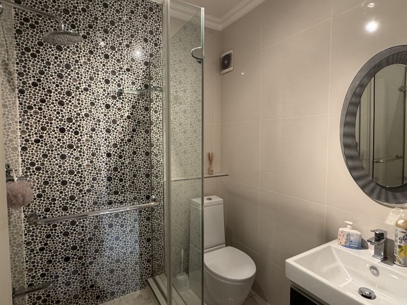 Modern bathroom featuring a walk-in shower with decorative mosaic tiling, a glass screen, a wall-mounted toilet, and a sleek vanity basin.