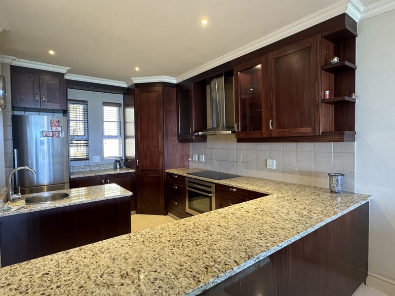 A well-appointed kitchen featuring dark wood cabinetry, granite countertops, a built-in oven, electric hob, and a stainless steel extractor fan.