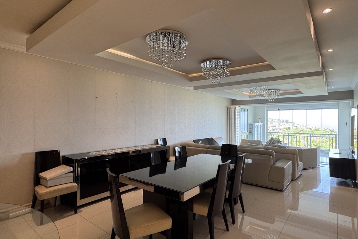 Spacious open-plan living and dining area featuring high-gloss floor tiles, recessed ceilings with crystal chandeliers, and large sliding doors leading to a balcony.